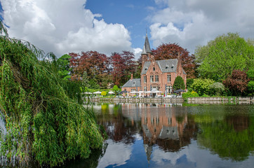 Fototapeta na wymiar View of tranquil public green space featuring Minnewater Lake and small castle in Bruges during sunny day in spring, Belgium
