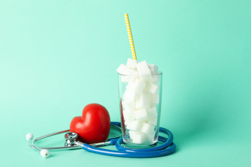 Glass with sugar cubes, heart and stethoscope on mint background