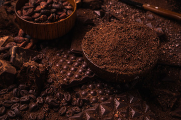 Cocoa beans, cocoa powder, cocoa butter, chocolate bar and chocolate sauce, chocolate bar in a wooden bowl on a dark background place for text