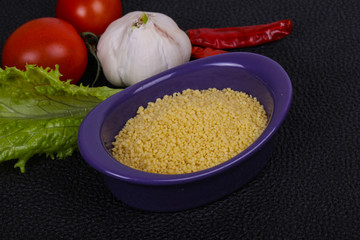 Raw couscous in the bowl served salad leaves, tomato and pepper
