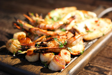 Fried prawns shrimps, squid and scallops with herbs, pepper and spices on wooden board.  Summer picnic, sunny day. Background image, copy space