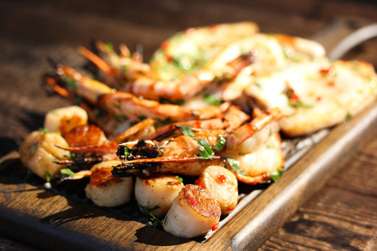 Fried prawns shrimps, squid and scallops with herbs, pepper and spices on wooden board.  Summer picnic, sunny day. Background image, copy space