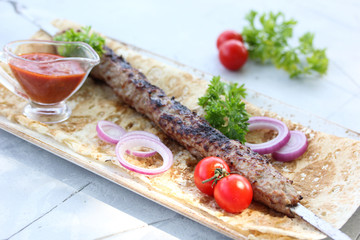 Fried lula kebab on a skewer on pita bread with parsley, onion rings, cherry tomatoes and ketchup on a light table. Meat on the grill. Background image, copy space