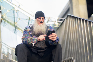 Happy mature bearded hipster man using phone at footbridge