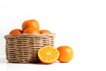 Many fresh oranges in a wooden basket placed on the floor. There are some balls that are cut in half to make them look appetizing. Healthy food concept, vitamin C, copy space. white background