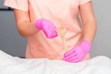 Cosmetologist hands are holding liquid sugar paste or wax during depilation procedure in salon.