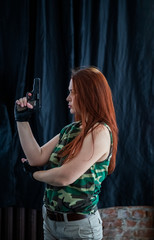 beautiful girl with red hair in military style posing with a gun