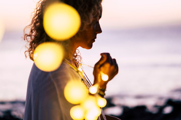 Emotional concept of hope and faith with adult woman and yellow bulb lights defocused - ocean and...