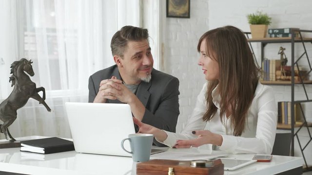 Happy business people working at desk using laptop computer, talking, working together - 4K video footage