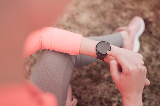 Fit Woman Checking Smart Watch Wearable Technology Sport Smartwatch On Fitness Run Walk Outside. Top View From Above With Running Shoes In Grass. Runner Girl Athlete Checking Heart Rate On Smartwatch.