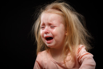 A little girl is crying hysterically in a dark room. She was badly hurt.