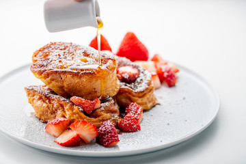 French toast with fresh strawberries and honey syrup on white plate.
Delicious dessert image.
