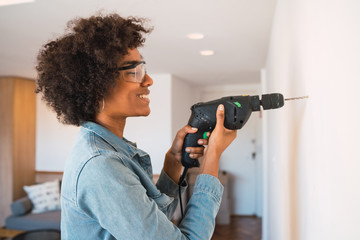 Afro woman drilling wall with electric drill. - obrazy, fototapety, plakaty