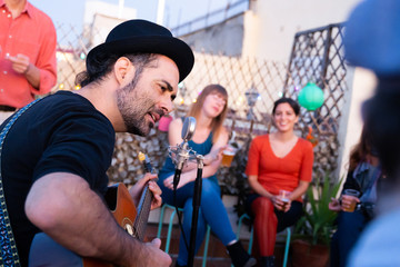 Lead singer of a rock band singing for audience on a rooftop. Portrait of a hipster male musician...