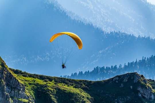 Yellow paraglider fly over mountain slope on sunny summer day,