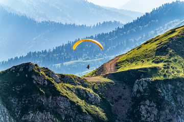 Yellow paraglider fly over mountain slope on sunny summer day,
