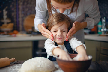 Young woman in formal clothing having fun while making dough with little adorable girl in modern...