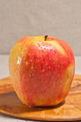 Front view, close up, of a single, ripe Ambrsa apple, on a rare wood plate