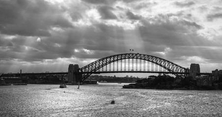 Panoramic view of the Sydney Harbour Bridge under a dramatic day, black and white.