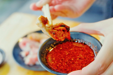 The hand is used to hold the chopsticks to bring the grilled pork to dip in tasty sauce. Sliced pork grill with sauce in barbecue shop.Close up.