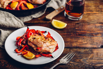 Oven baked chicken thighs with red bell peppers and lemon on white plate.