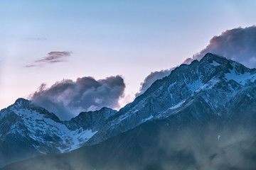 High mountains with snowy peaks at sunset in clouds and fog