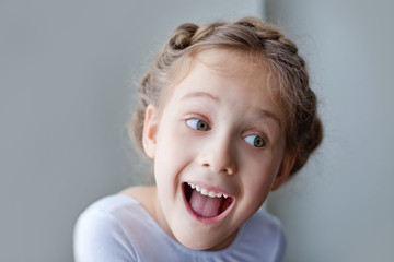 Large portrait of a little girl. Looking at the camera, she is genuinely, happily giggles-smiles. On a gray background.