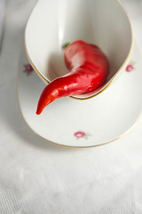 Red pepper capi in a porcelain sauce cup on a white tablecloth in the morning light. Copy space.
