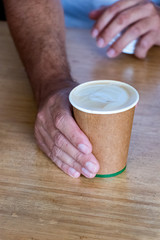 Male barista hand serving a cappuccino on a cup recycled disposable paper.