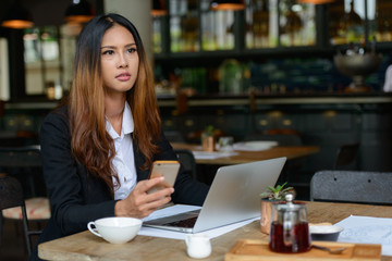 Young beautiful Asian businesswoman using phone at the coffee shop