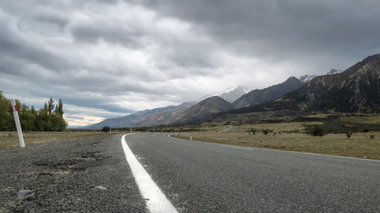Road leading towards mountains, with cloudy sky. Low perspective shot made in Aoraki / Mt Cook National Park in New Zealand.