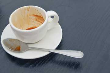 Dirty coffee cup on black wood table in cafe shop.Coffee drink on woode.n table.lose up view of cup of coffee on saucer.Close up.