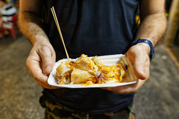 Male hands holding grilled stuffed squid at Phu Quoc night market, Vietnam 