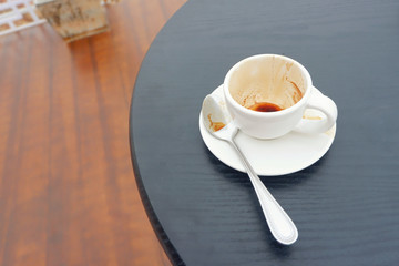 Empty and dirty white tea cup on wood table in cafe.Tea cup with spoon on black wood table,Close up.