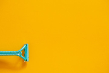Blue razor on a yellow background top view. The concept of hygiene, beauty, shaving.