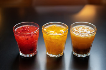 Three multi-colored drinks of fruit and berry juice on a black table with a sun glare.