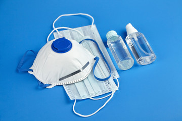 Antibacterial hand sanitizer, respirator and surgical masks on blue background