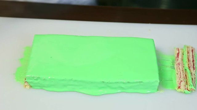 confectioner puts small slices of layered cake next to big green glazed rectangle
