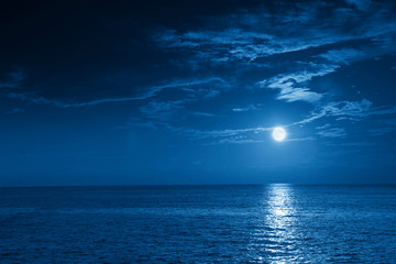 Fototapeta na wymiar This photo illustration of a deep blue moonlit ocean and sky at night would make a great travel background for any travel or vacation purpose.