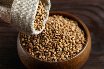 Buckwheat groats (hulled seeds) in bowl and burlap bag on wooden table