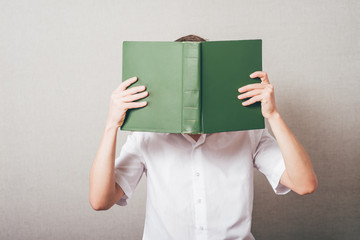The man in glasses covered his face with a book. On a gray background. - 340028986