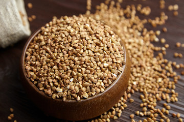 Buckwheat groats (hulled seeds) in bowl and burlap bag on wooden table