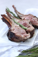 Grilled lamb ribs with rosemary and spices on a white plate on a light table. Background image, copy space
