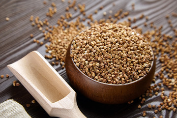 Buckwheat groats (hulled seeds) in bowl, wooden scoop, closeup