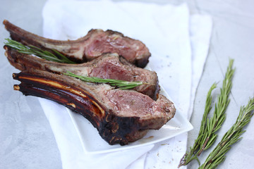 Grilled lamb ribs with rosemary and spices on a white plate on a light table. Background image, copy space