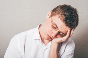 The man in glasses tired sleep. On a gray background.