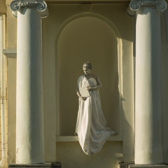 Live sculpture of a young woman pregnant in full growth, against the background of a yellow building with white columns