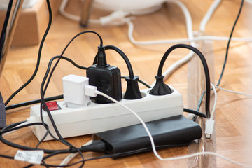 Messy outlet power extension cord on an apartment floor with various charging devices plugged in