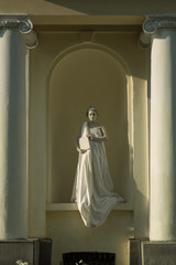 Live sculpture of a young woman pregnant in a long white dress with a book, full-length, against the background of a yellow building with white columns