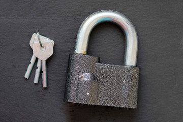 A padlock with a thick handle and three steel keys. Large padlock on a black background top view....
